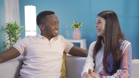 Happy-african-young-man-and-his-caucasian-girlfriend-chatting-and-smiling-at-home